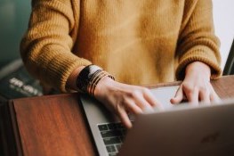 A girl typing on a silver laptop that is on her lap